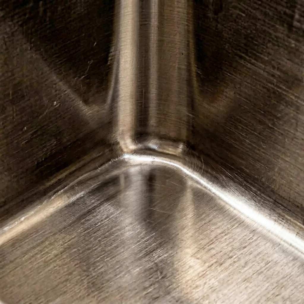 Macro close-up of seamless hydraulic press-drawn corner in AISI 304 stainless steel sink